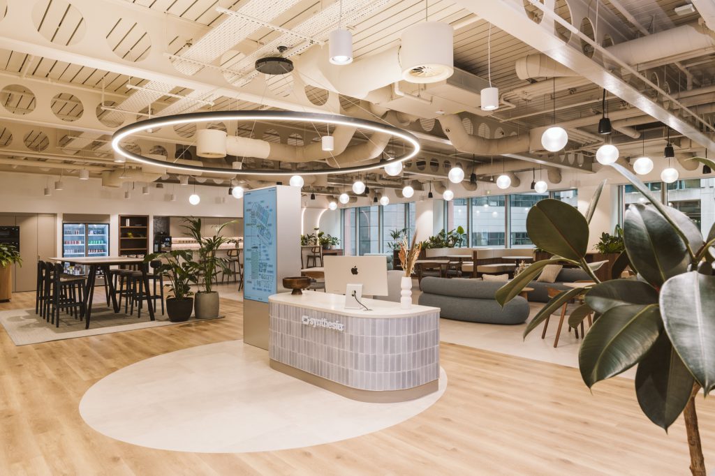 Reception desk and digital totem with drinks fridges and high tables to one side, lounge seating to the other