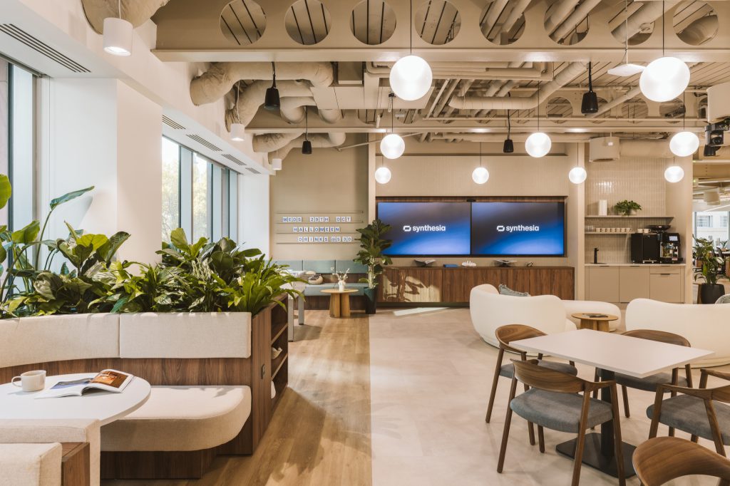 Curved banquette and planters facing twin screens and a letterboard, coffee point alongside