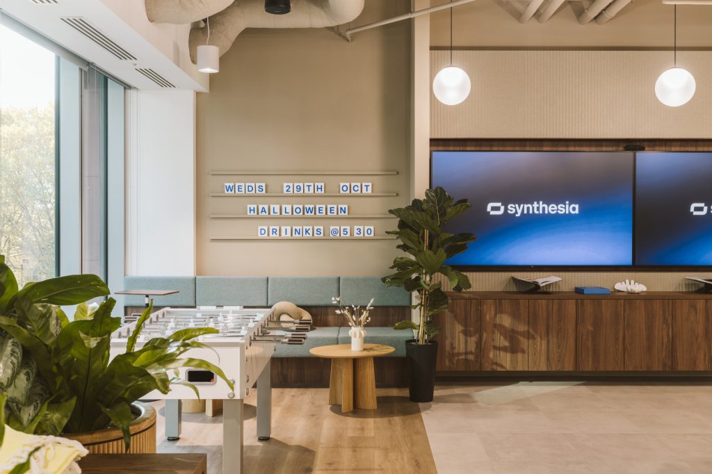 Foosball table and mint banquette beneath a letterboard and twin branded screens