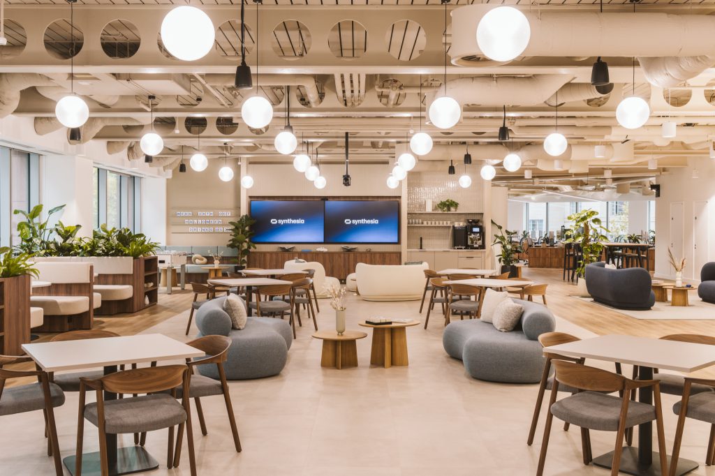 Pebble-shaped sofas and cafe tables under a field of globe pendants, the pantry bar beyond