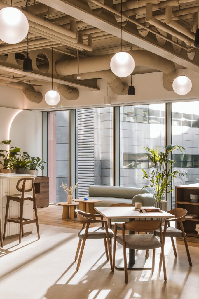 Coffee bar with rattan-backed stools beside a sage sofa and palms, an arched light glowing on the wall
