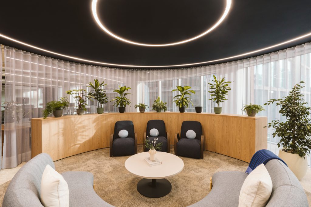 Circular lounge under two glowing light rings, navy armchairs and curved sofas around a round table