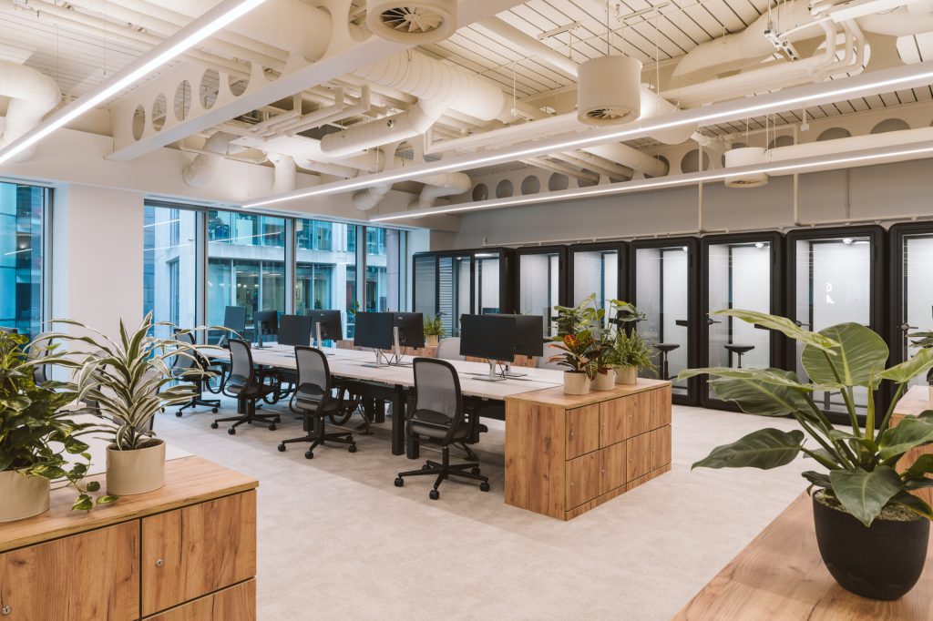 Open workspace with sit-stand desks and timber lockers, a row of black phone booths along the wall
