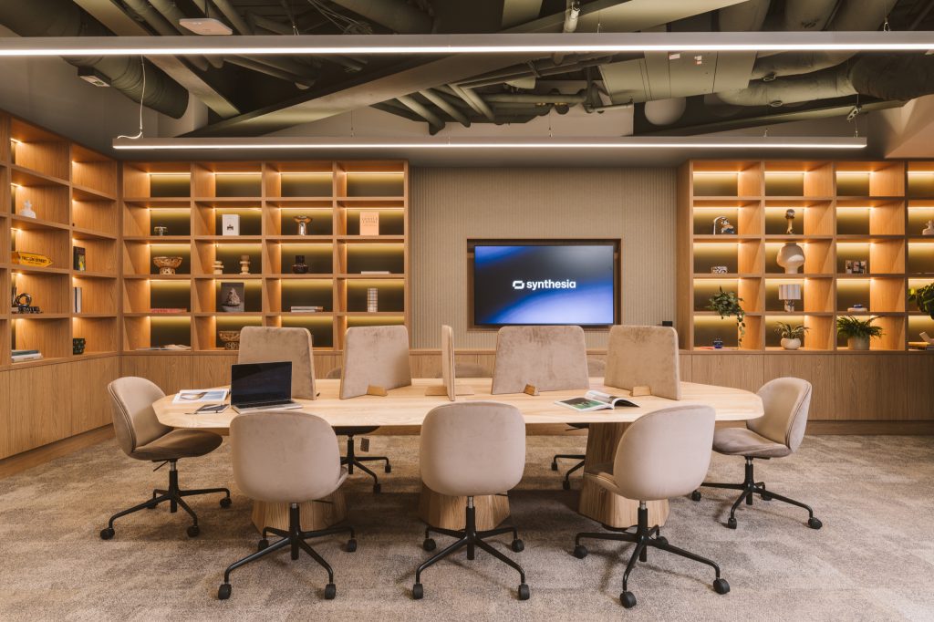 Communal ash table with felt privacy screens and velvet chairs between walls of backlit shelving