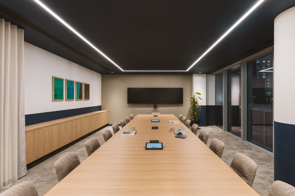 Boardroom with a long oak table, navy dado and dual screens beneath a rectangle of light